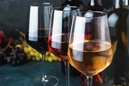 KI generiert: Drei Weingläser mit Rot-, Rosé- und Weißwein, im Hintergrund Trauben und Weinflaschen.