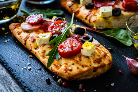 Focaccia mit Tomaten, Feta, Salami und Oliven auf Schieferplatte angerichtet.