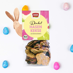Packung von Dinkel-Hasenkeksen mit Vollmilchschokolade, umgeben von bunt gefärbten Eiern.