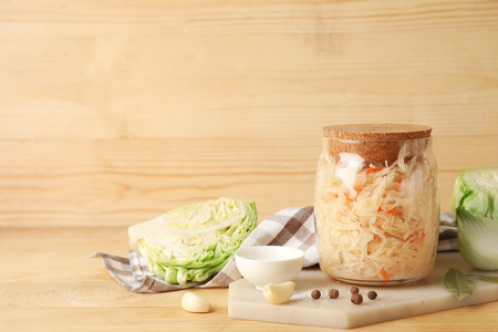 KI generiert:  Ein Glas Sauerkraut mit Pfefferkörnern und Knoblauch auf einem Holzbrett.