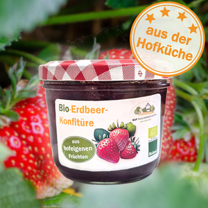 Ein Glas Bio-Erdbeerkonfitüre vor Erdbeeren, Aufschrift: "aus hofeigenen Früchten", "aus der Hofküche".