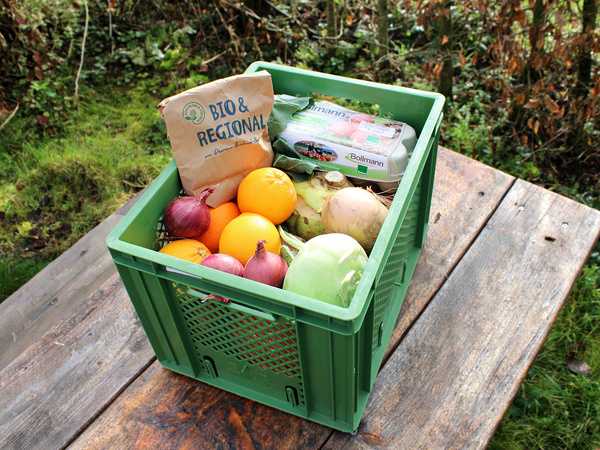 KI generiert: Grüne Kiste mit Gemüse, Obst und Eiern auf Holztisch. Text: "BIO & REGIONAL".