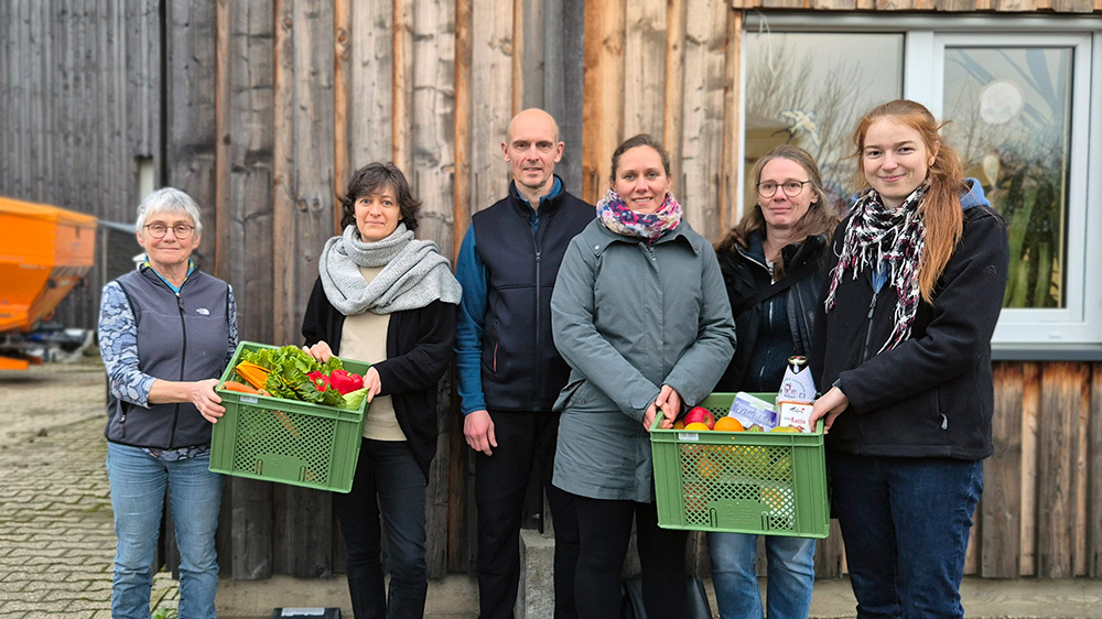 KI generiert: Sechs Personen posieren mit Gemüse- und Obstkisten vor einem Holzgebäude.