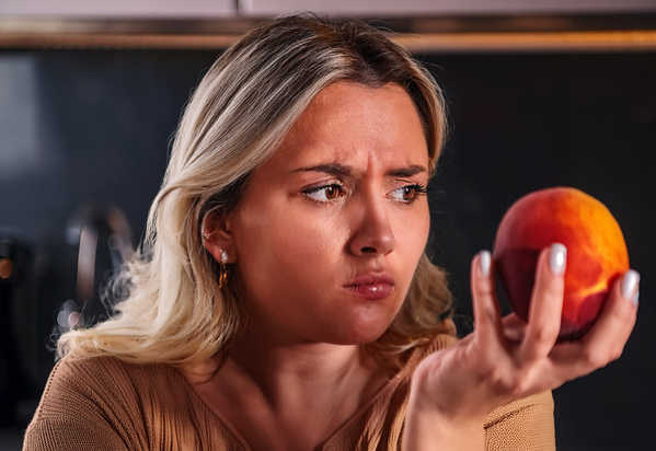 KI generiert: Eine Frau blickt nachdenklich auf einen Pfirsich in ihrer Hand.