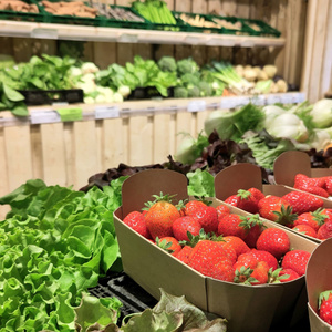 Erdbeeren in Pappschalen, umgeben von frischem Grünzeug im Laden.