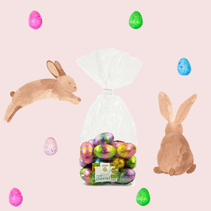 Packung von Dinkel-Hasenkeksen mit Vollmilchschokolade, umgeben von bunt gefärbten Eiern.