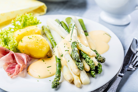 Ein Teller mit grünem und weißem Spargel, Schinken, Kartoffeln und Soße.