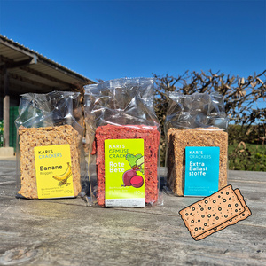 Drei Packungen Kari's Crackers mit unterschiedlichen Zutaten auf einem Holztisch. Texte: "Banane", "Rote Bete", "Extra Ballaststoffe".