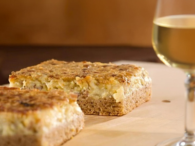 Stimmungsvoll dekorierter Gartentisch mit Wein, Käse und Lichterketten unter einem Baum.