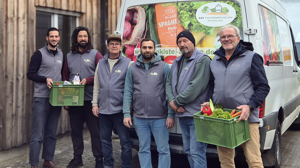 KI generiert: Gruppe von sechs Männern vor einem Lieferwagen mit Gemüsekisten. Text am Wagen: "www.oekokiste".