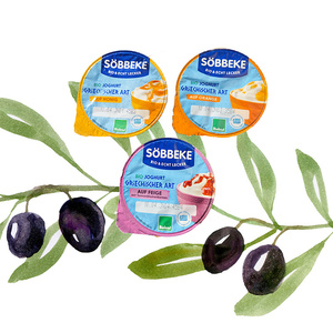 Drei Becher Söbbeke Bio Joghurt griechischer Art vor einem Hintergrund mit Olivenzweigen.