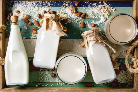 KI generiert: Verschiedene Flaschen und Gläser mit pflanzlicher Milch, umgeben von Mandeln und Hafer.