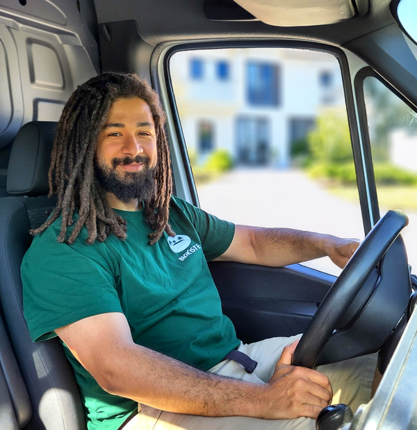 KI generiert: Ein Mann sitzt lächelnd in einem Lieferwagen und trägt ein grünes "Ökokiste"-Shirt.