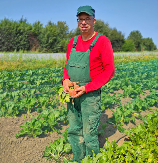 Ein Landwirt steht auf einem Feld und hält frisches Gemüse in den Händen.