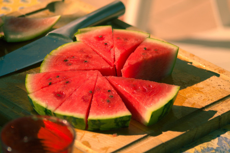 Geschnittene Wassermelone auf einem Holzbrett mit einem Messer daneben.