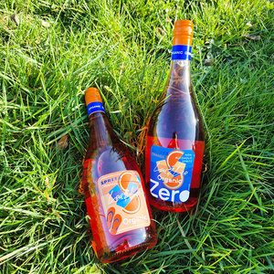 Zwei Flaschen Lou Lou Organic Spritz Orange im Gras. Text: "Lou Lou Organic Spritz Orange Zero".