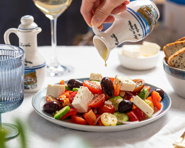 Stimmungsvoll dekorierter Gartentisch mit Wein, Käse und Lichterketten unter einem Baum.