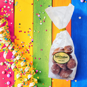 Eine Tüte mit Gebäck vor buntem Hintergrund und Konfetti. Text: "Schomaker Die BIObäckerei 150% BIO".