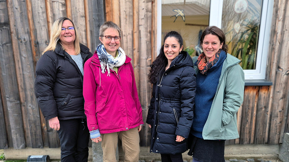 KI generiert: Vier Personen stehen lächelnd vor einem Holzgebäude.