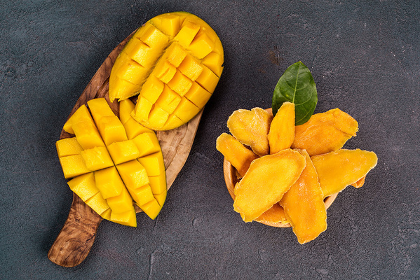 KI generiert: Frische Mangostücke und getrocknete Mangoscheiben auf einem Holzbrett und in einer Schüssel.