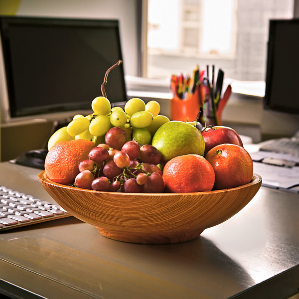 Eine Holzschale mit verschiedenen Früchten steht auf einem Schreibtisch im Büro.