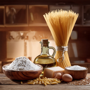 Zutaten für Pasta: Spaghetti, Mehl, Öl, Eier und Parmesan auf einem Holztisch arrangiert.