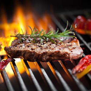 Ein Steak mit Rosmarin auf dem Grill über offener Flamme.